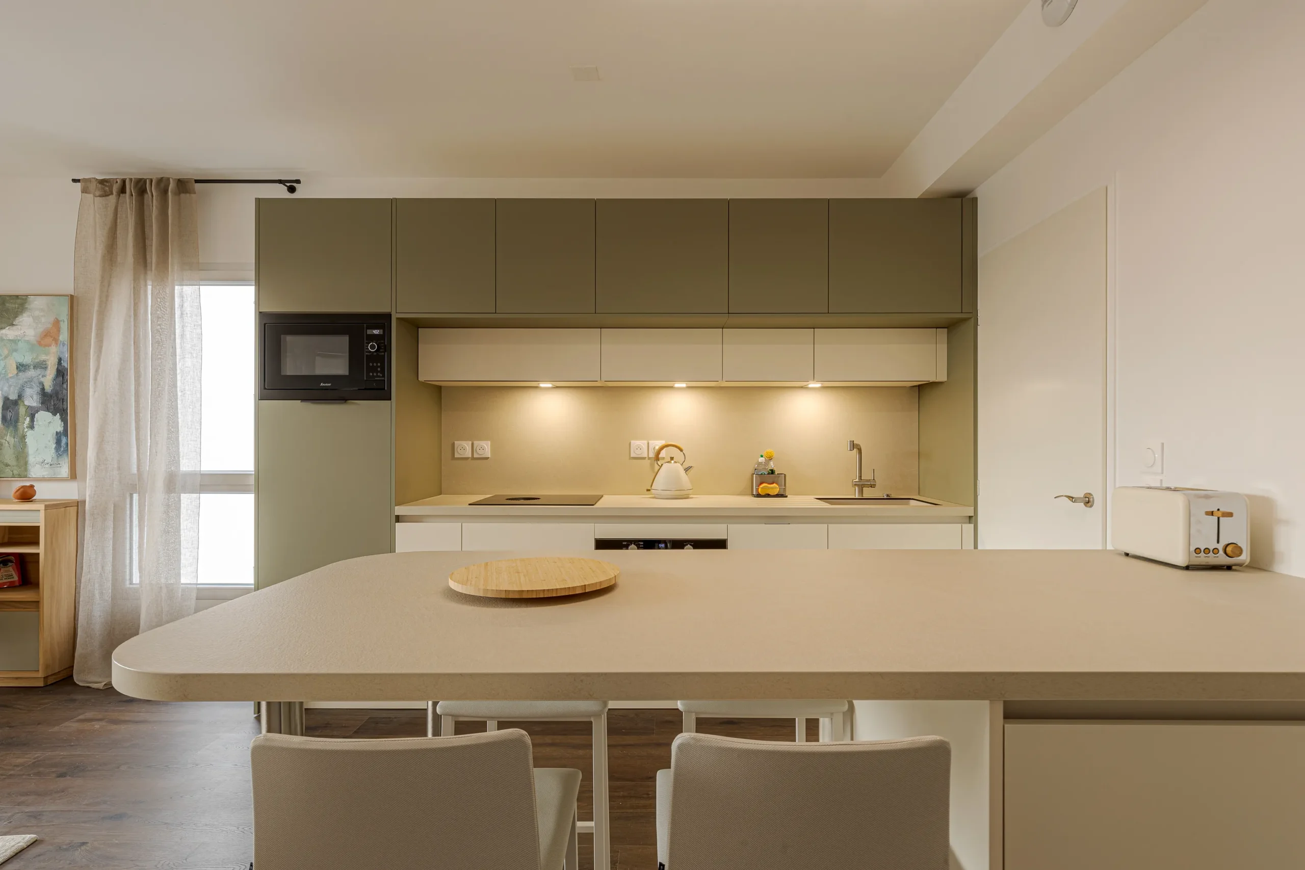 Cuisine sur mesure avec coin repas attenant, rangements muraux vert sauge et façades blanches