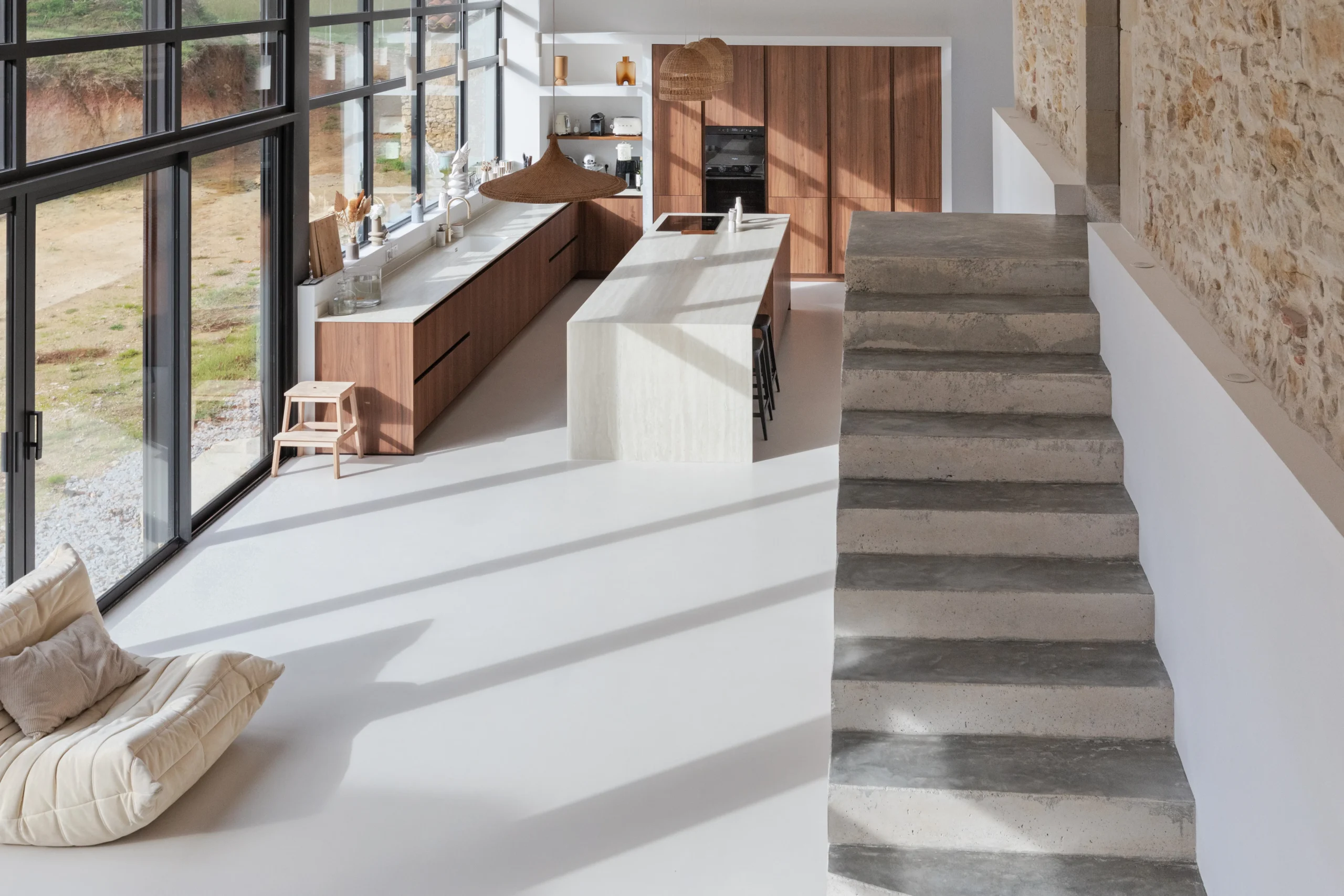 Cuisine avec îlot central, façades en décor bois, escalier clair et mur en pierre apparente