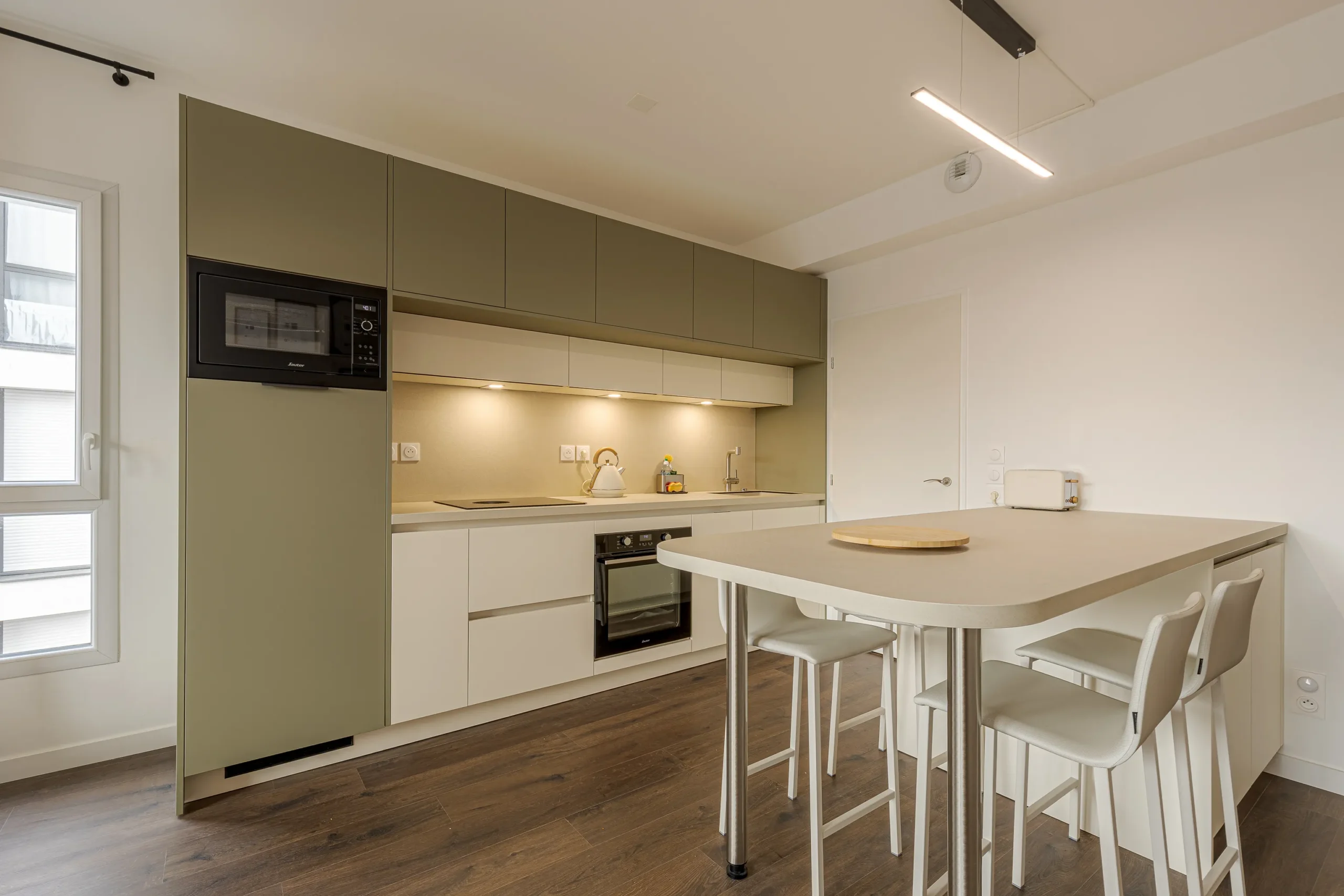 Vue d’ensemble d’une cuisine sur mesure avec table snack, rangements intégrés et assises hautes dans un intérieur compact