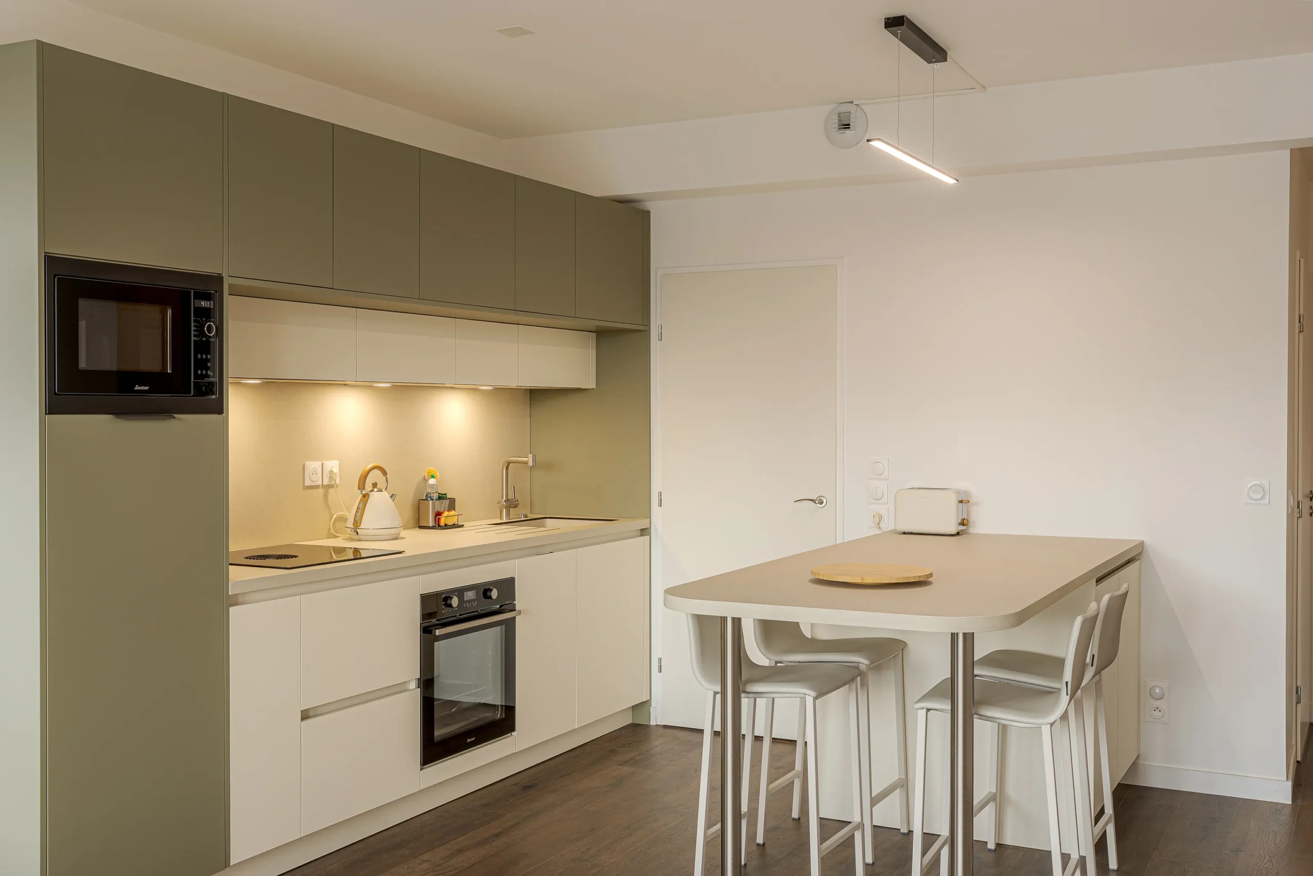 Cuisine sur mesure ouverte avec table snack, façades vert sauge et blanches, et circulation dégagée