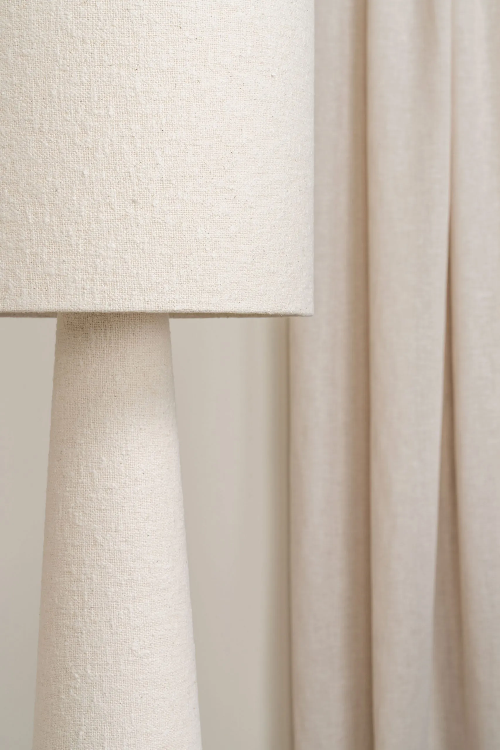 Détail d’un abat-jour en tissu beige devant des rideaux clairs, pour une ambiance douce et chaleureuse.