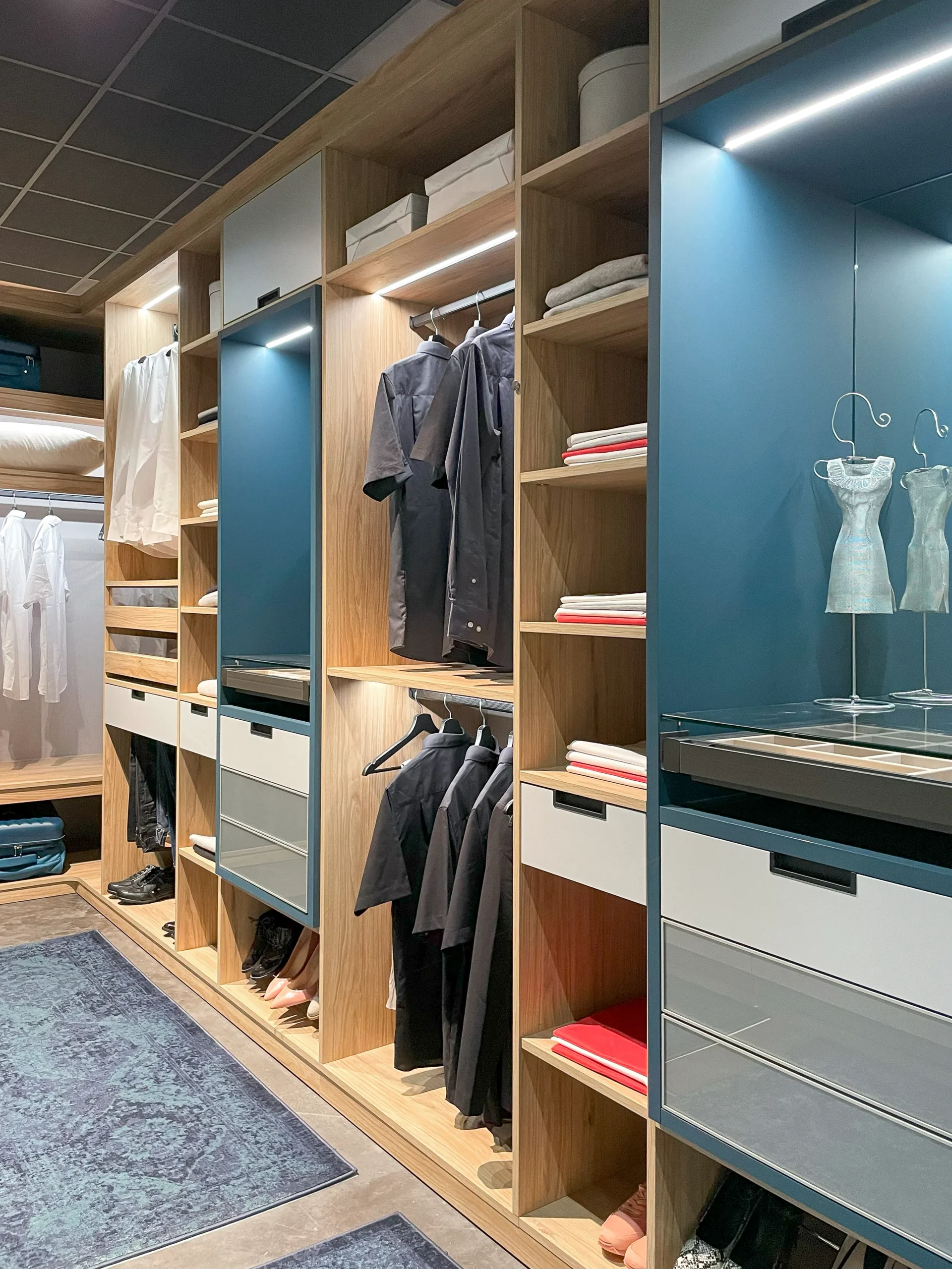 Dressing ouvert en bois clair avec penderie, étagères, tiroirs compartimentés et éclairage intégré pour une organisation soignée.