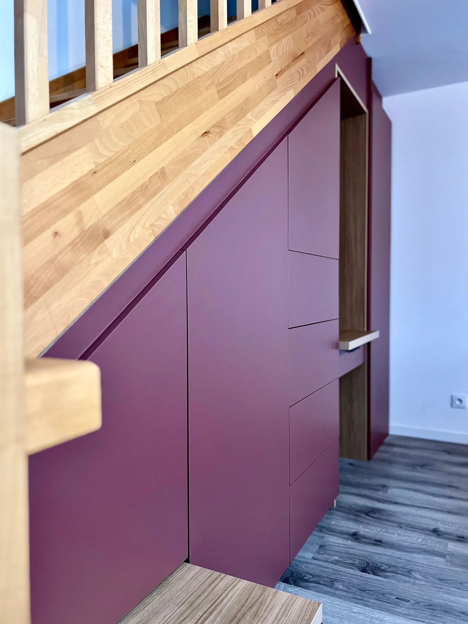 Aménagement sous escalier sur-mesure avec façades rose poudré, niches bois et garde-corps en bois naturel.