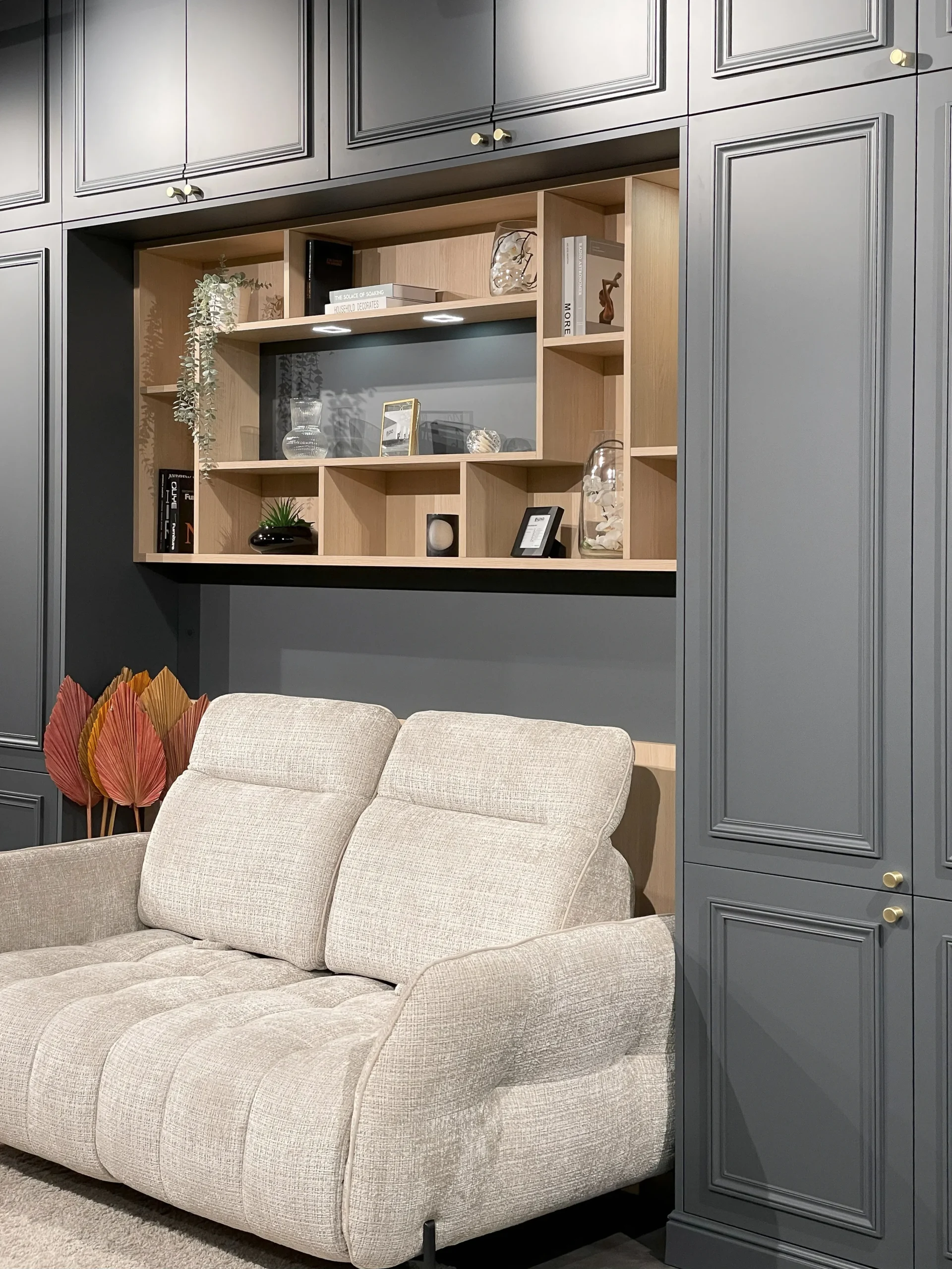 Niche bibliothèque en bois clair intégrée dans un meuble pont gris, avec étagères décoratives et éclairage discret.