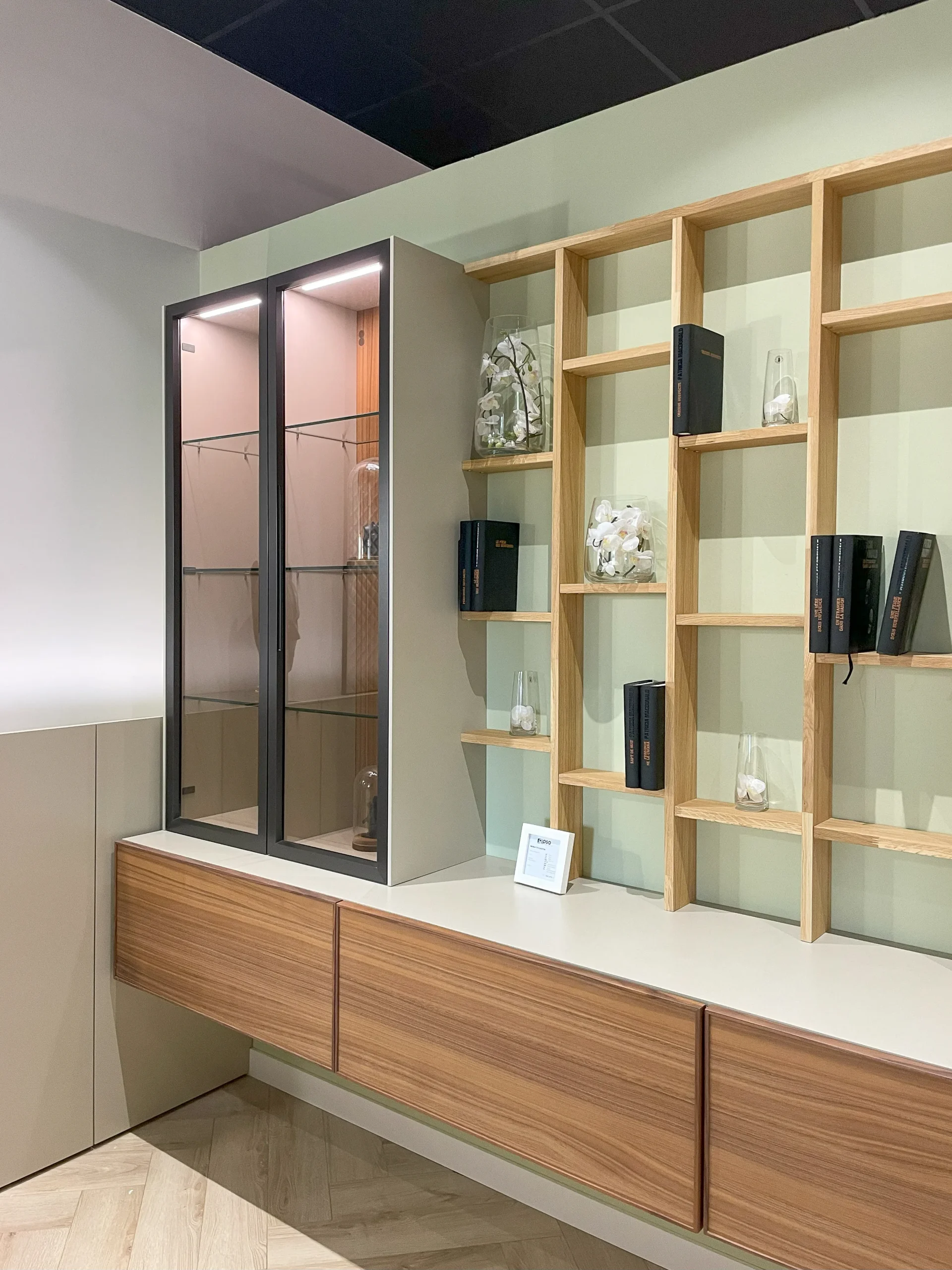 Bibliothèque sur-mesure en bois clair avec vitrine éclairée, niches ouvertes et meubles bas suspendus dans un espace chambre.