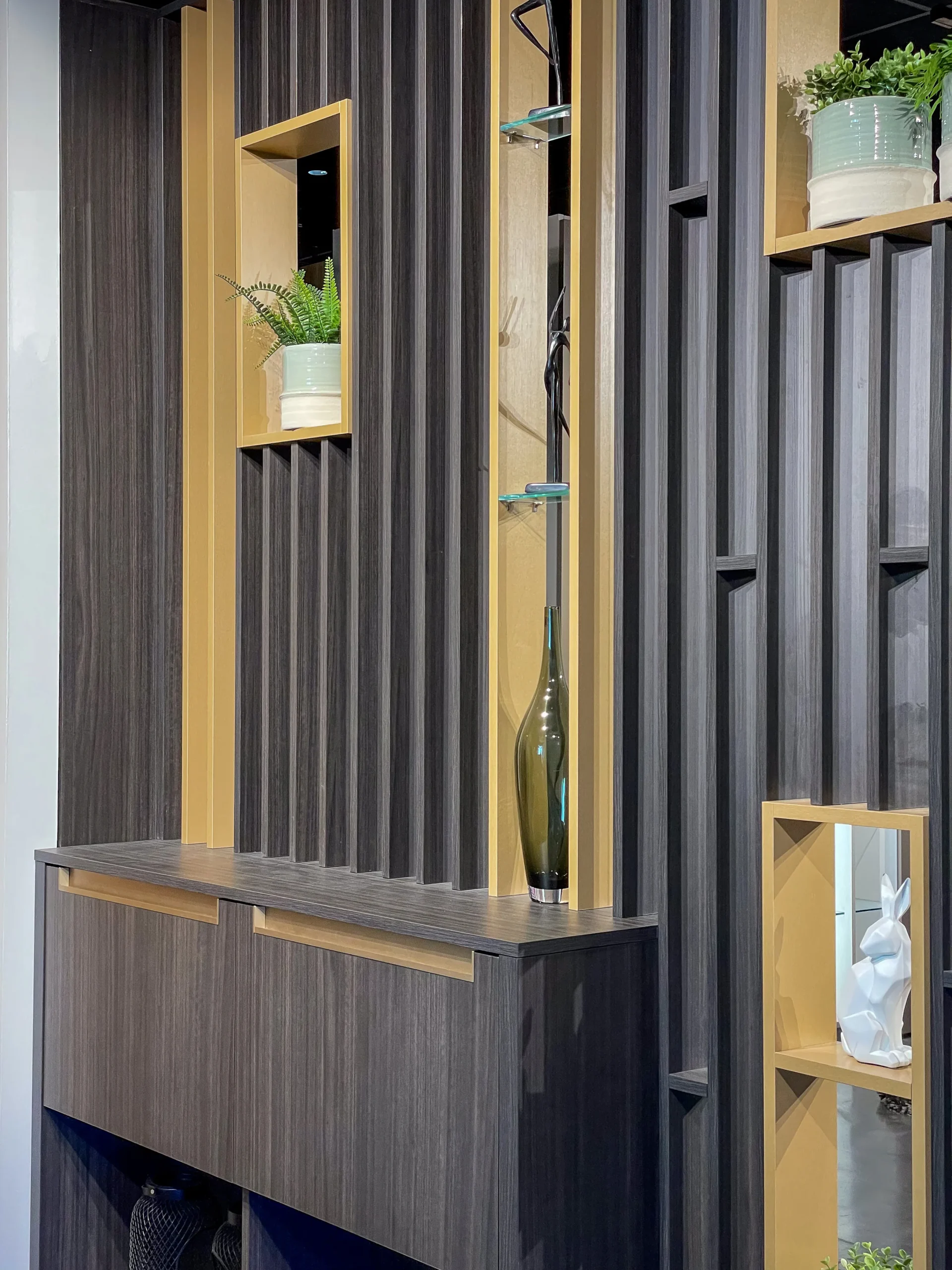 Détail d’un claustra intérieur en bois foncé avec console intégrée, niches décoratives, vase en verre et finitions bois clair contrastées.