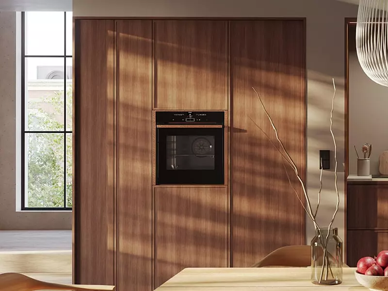 Colonnes de cuisine en bois noyer avec four encastré noir, façades verticales élégantes et lumière naturelle sur les finitions.