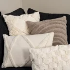 Assortiment de coussins blancs et beiges texturés sur canapé noir, pour une décoration chaleureuse et contemporaine.