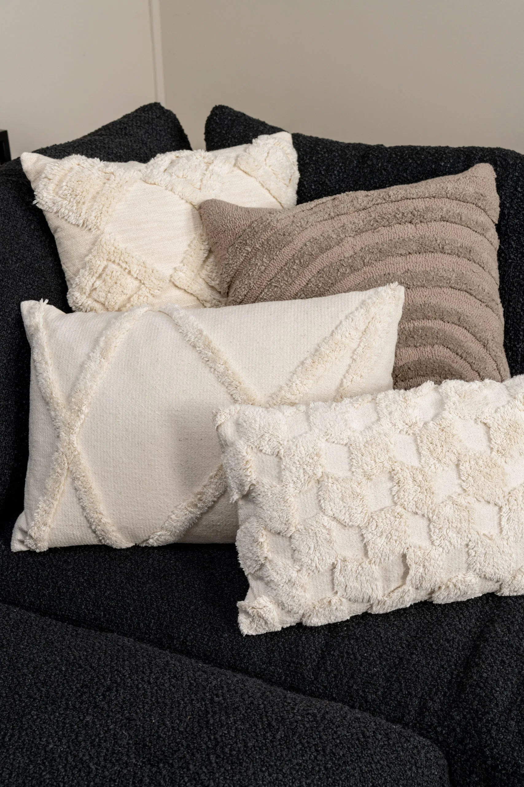 Assortiment de coussins blancs et beiges texturés sur canapé noir, pour une décoration chaleureuse et contemporaine.