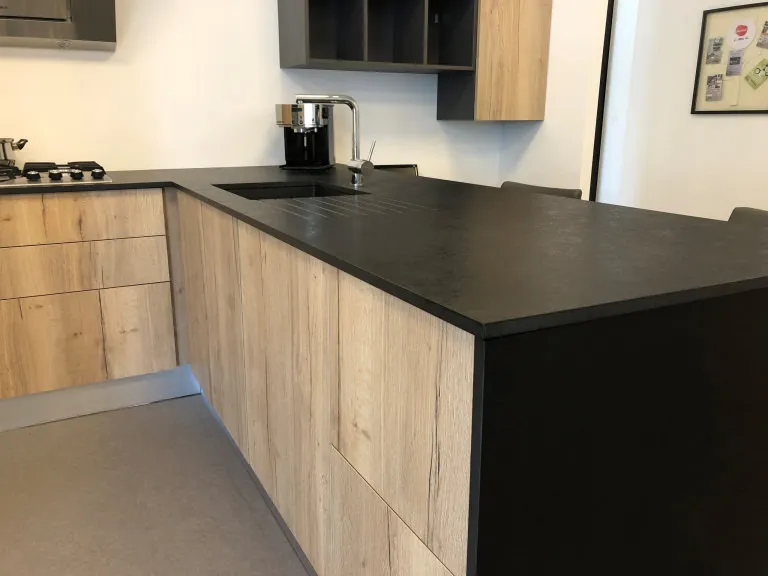 Cuisine compacte en bois clair avec plan de travail noir, évier intégré, rangements hauts et retour comptoir dans un showroom contemporain.