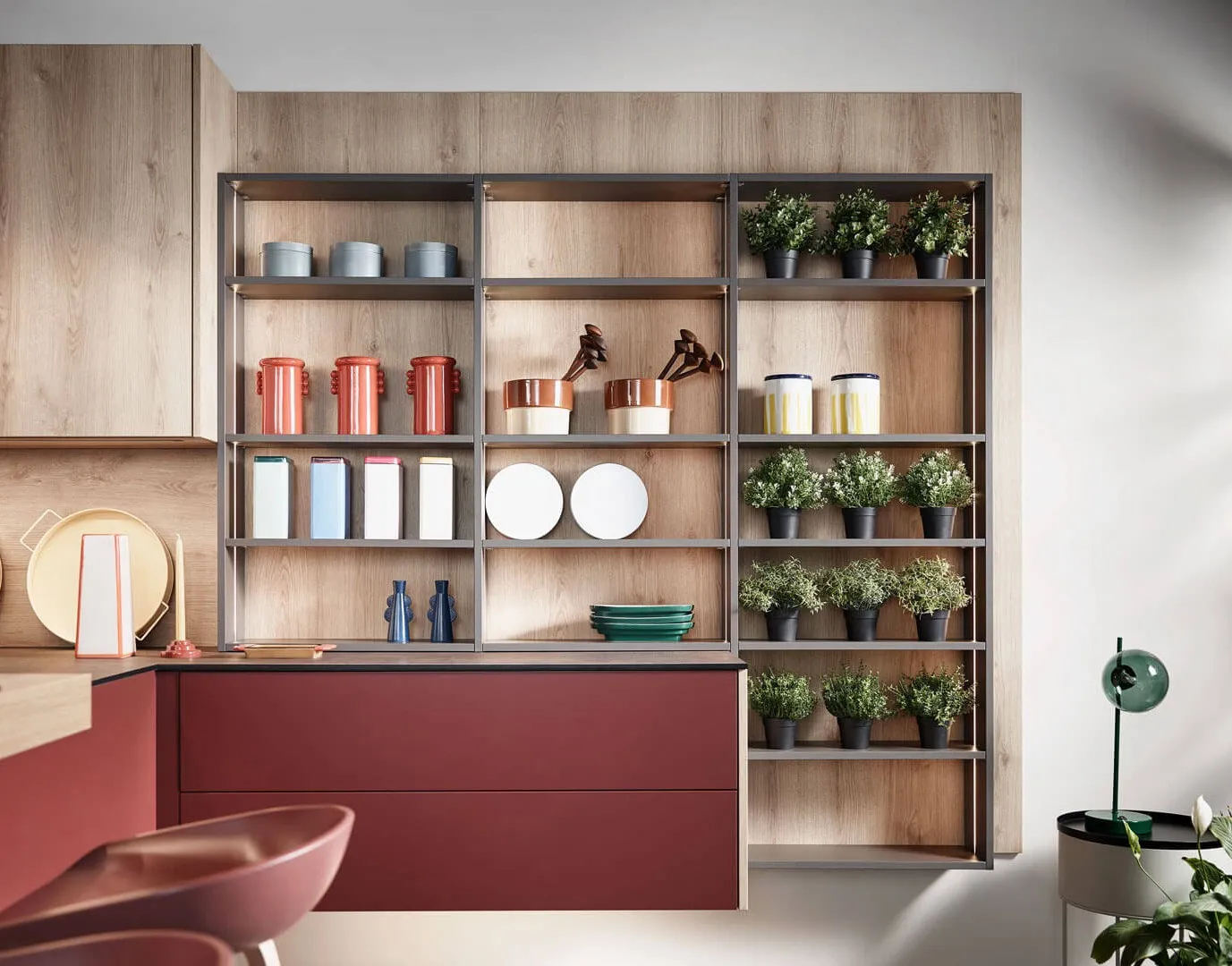 Cuisine bois clair et rouge avec étagères ouvertes, rangements décoratifs, plantes en pots et niches murales pour objets du quotidien.