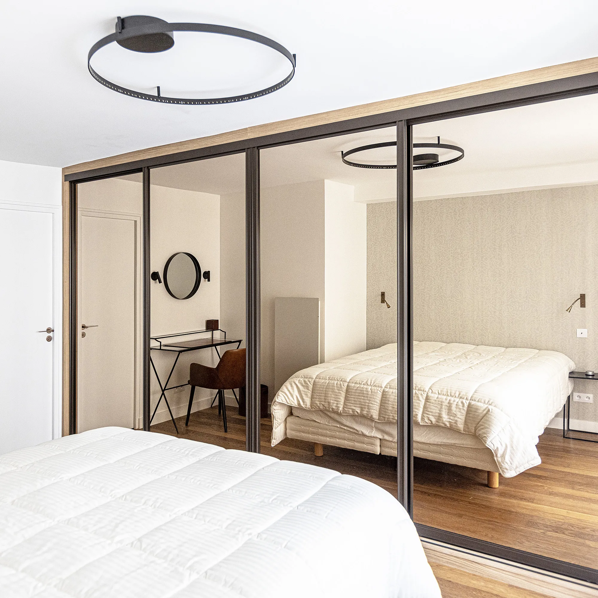 Dressing toute hauteur avec portes coulissantes miroir, profilés noirs et décor bois pour agrandir visuellement la chambre.