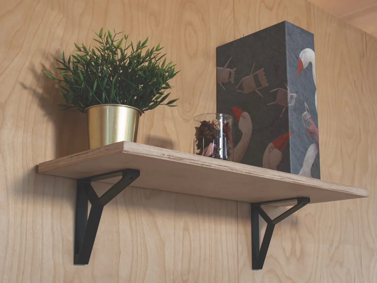 Étagère murale décor bois avec supports noirs, plante verte et objets décoratifs sur panneau mural effet bois.