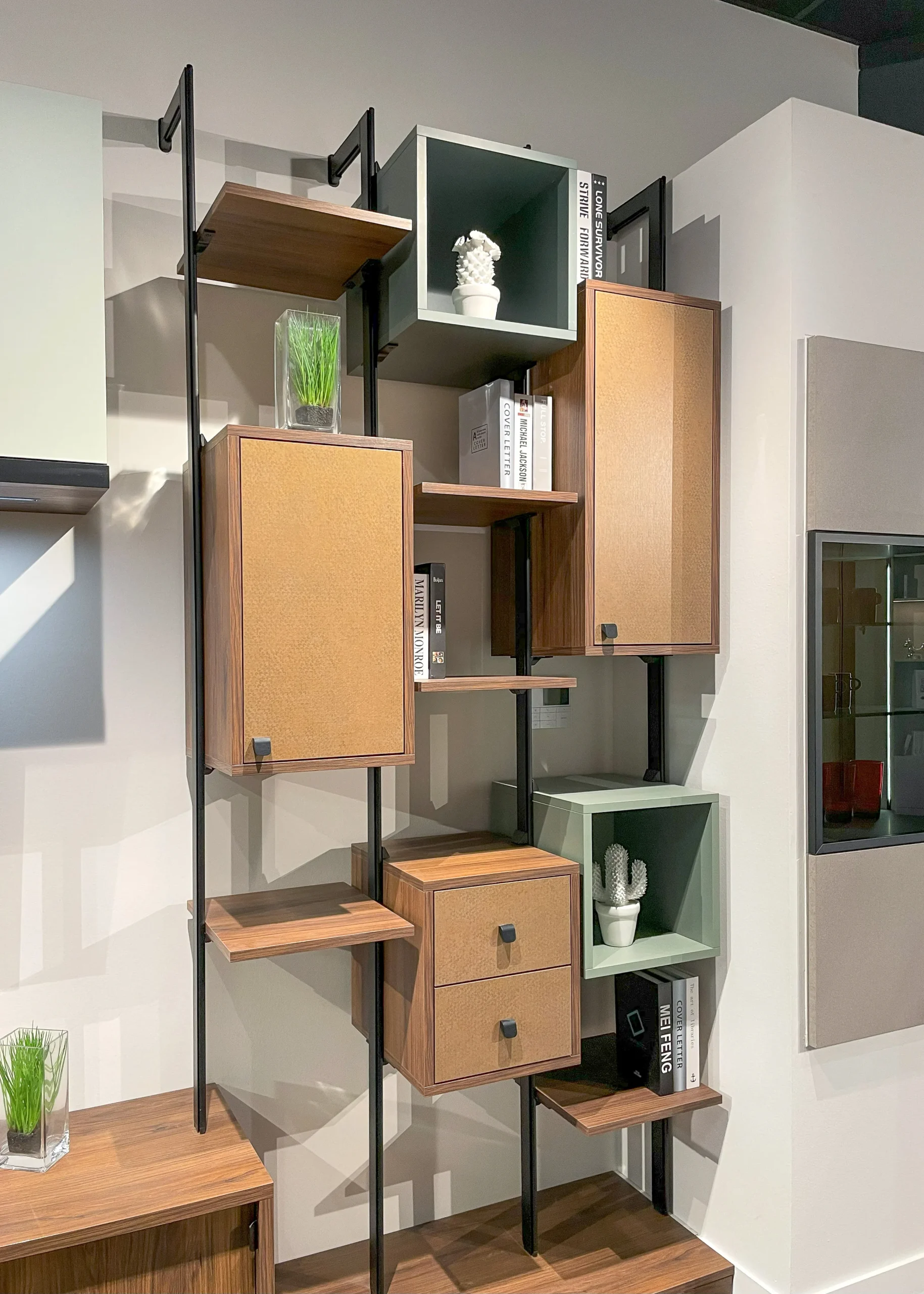 Détail d’un rangement mural sur-mesure avec caissons bois, tablettes ouvertes, structure noire et niches décoratives colorées.