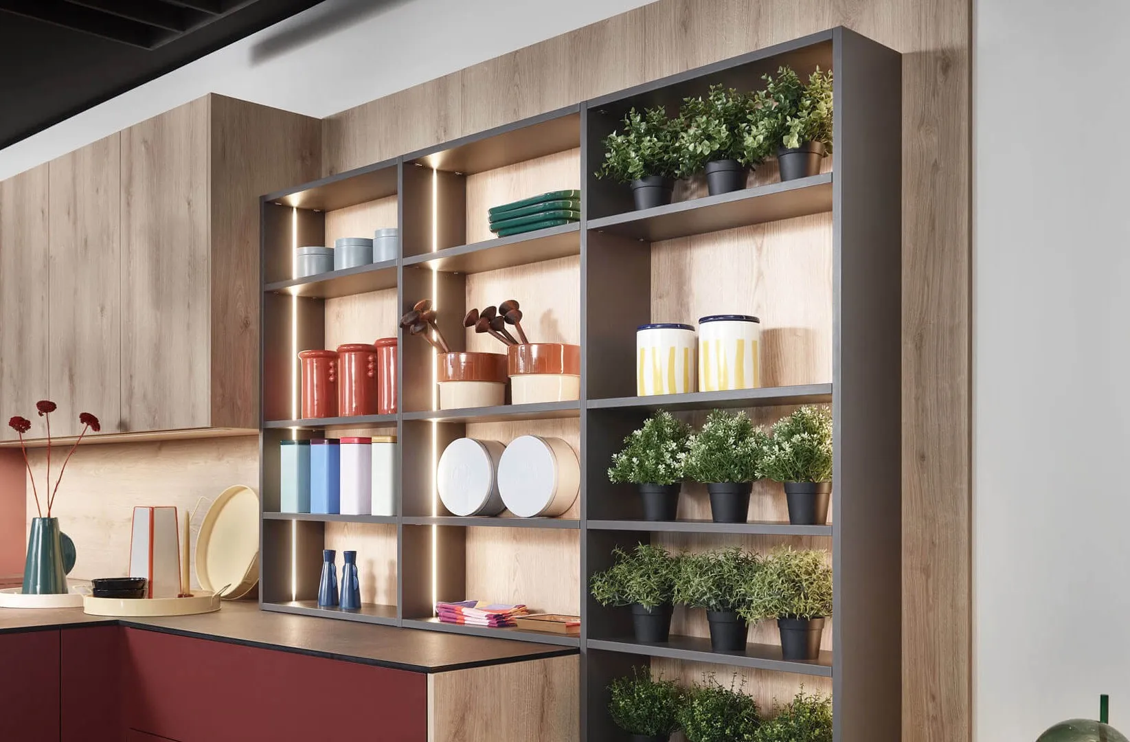 Étagères ouvertes dans une cuisine bois et terracotta, avec niches éclairées, plantes, vaisselle décorative et structure métallique.