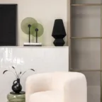 Fauteuil blanc bouclette dans un salon élégant avec table d’appoint, objets décoratifs et verrière en arrière-plan.