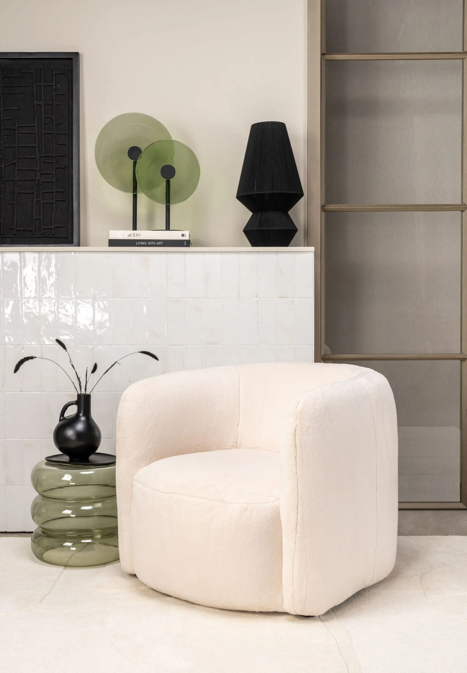 Fauteuil blanc bouclette dans un salon élégant avec table d’appoint, objets décoratifs et verrière en arrière-plan.