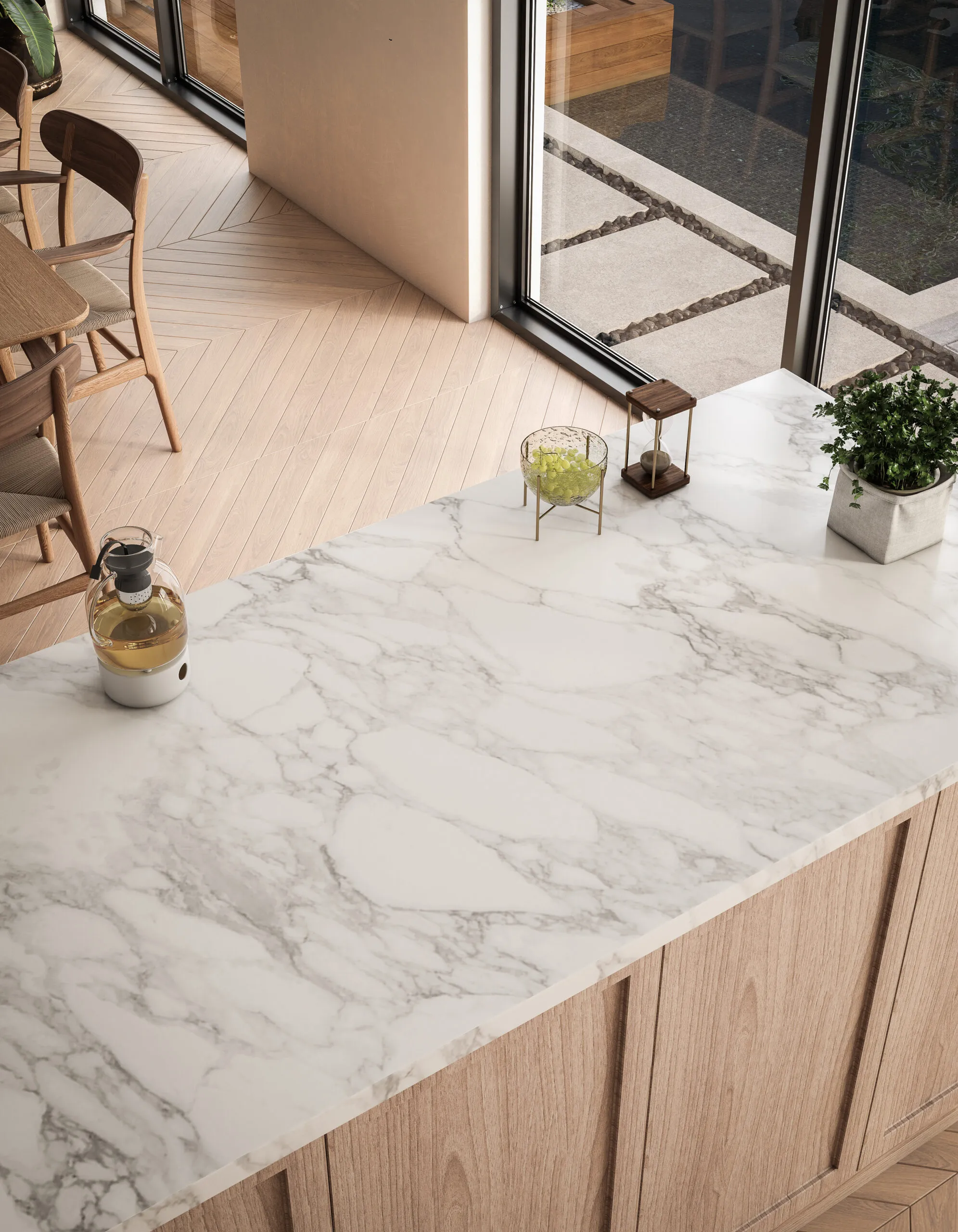 Îlot de cuisine avec plan de travail effet marbre blanc, façades bois clair, grande baie vitrée et sol en parquet à motif chevron.