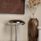 Lampe de table chromée avec vase ambré et décor mural texturé dans une mise en scène élégante et contemporaine.