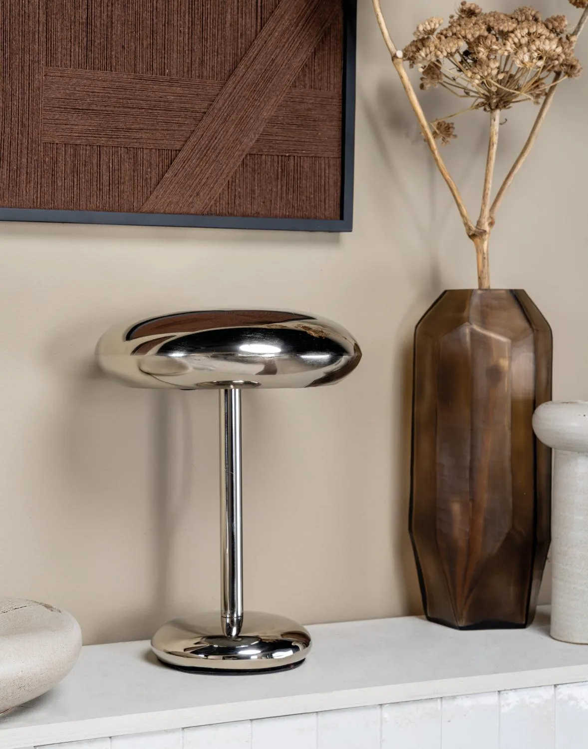 Lampe de table chromée avec vase ambré et décor mural texturé dans une mise en scène élégante et contemporaine.