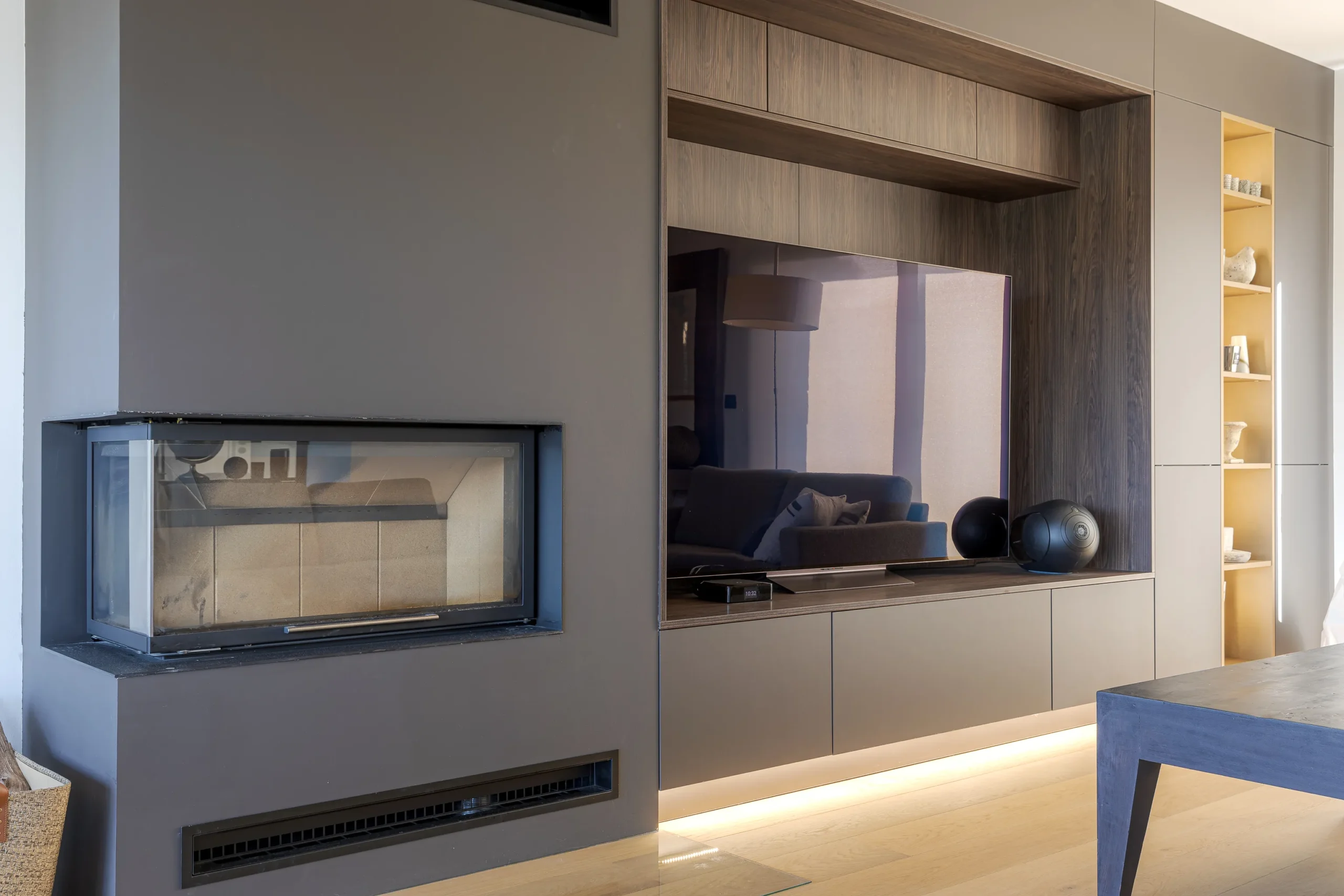 Aménagement TV sur mesure associant façades mates, décor bois foncé, éclairage indirect et cheminée intégrée au mur.