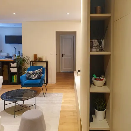 Aménagement sur-mesure combinant meuble TV, rangements d’entrée, étagères ouvertes et finitions beige et bois.