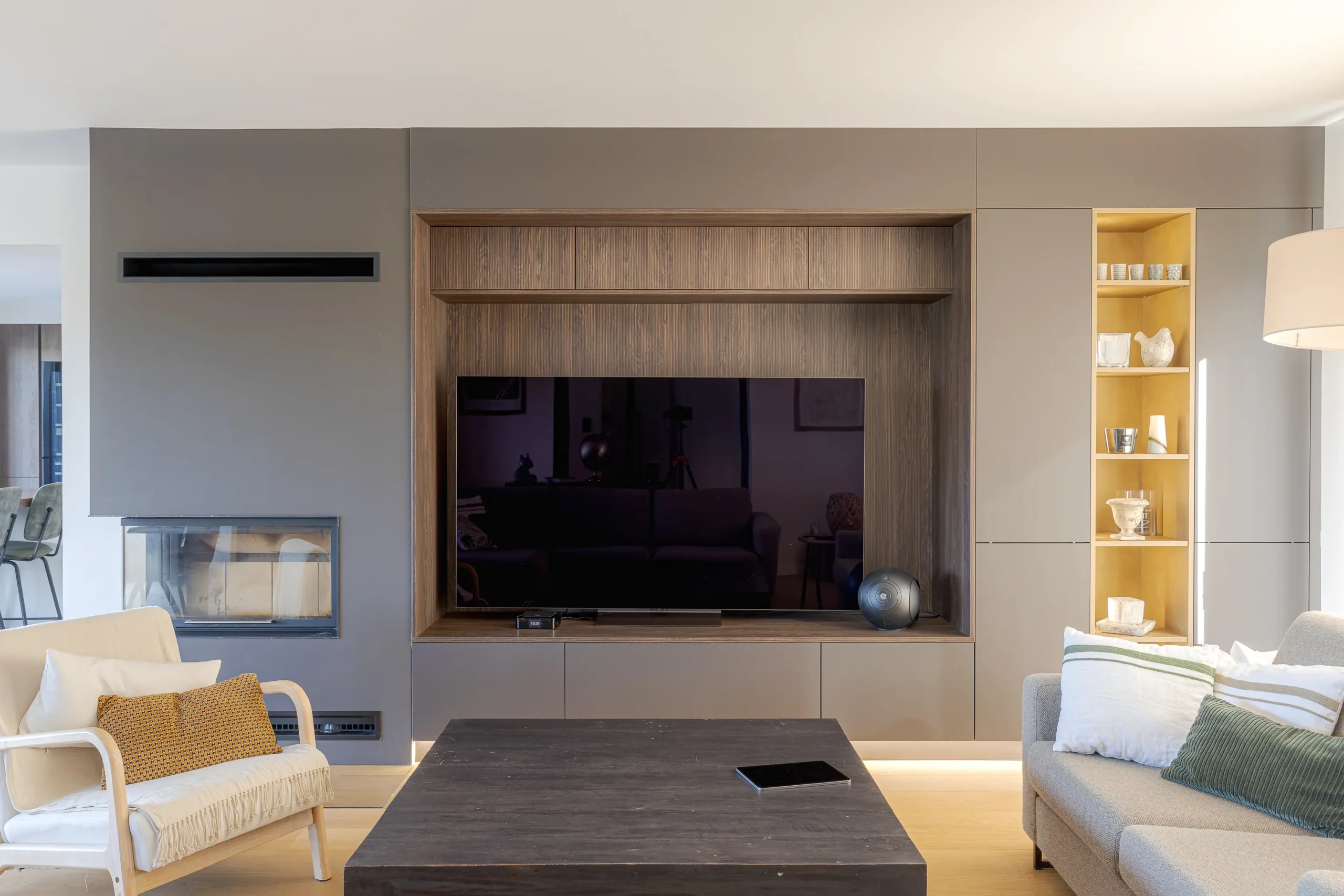 Meuble TV mural sur mesure avec encadrement bois, façades taupe, cheminée latérale et étagère décorative rétroéclairée.