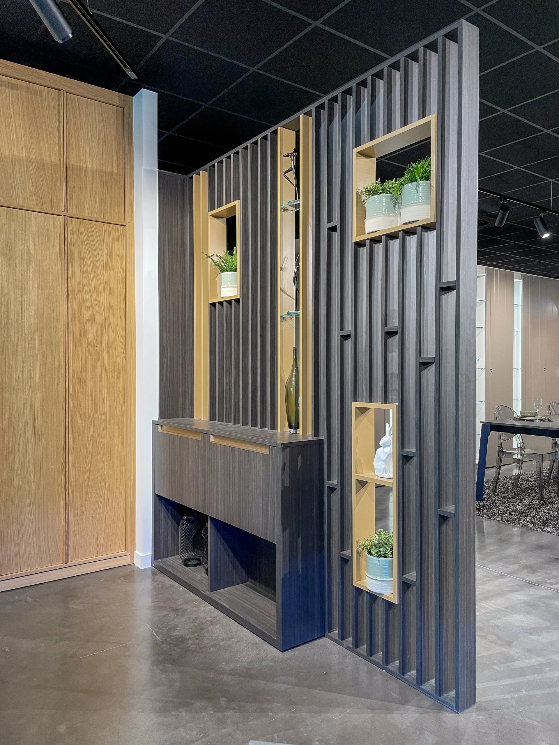 Meuble séparateur sur-mesure en bois foncé avec claustra vertical, rangements bas, niches ouvertes et touches bois clair décoratives.
