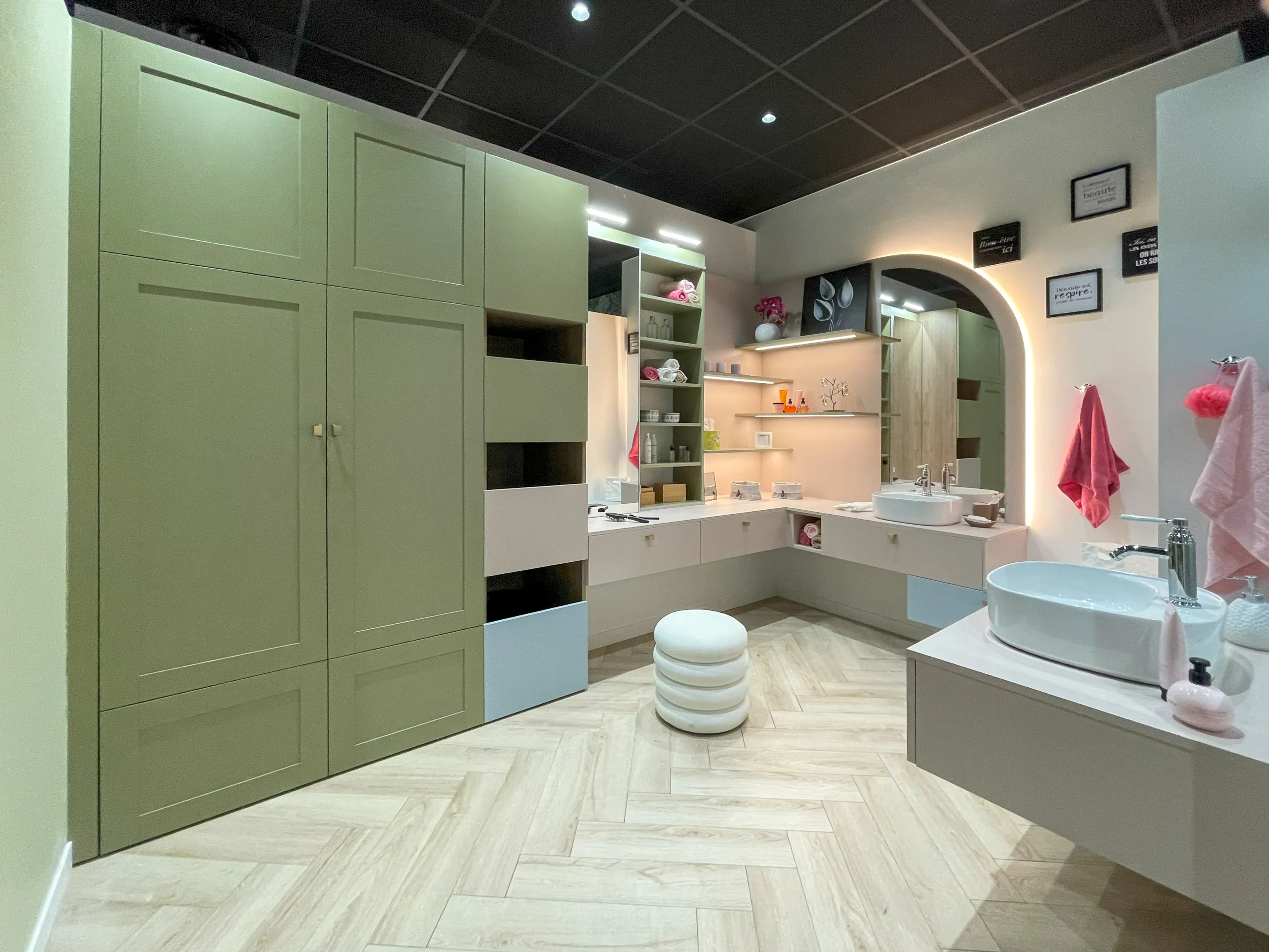 Salle de bain avec meubles sur-mesure vert sauge, miroir arrondi, vasques posées et nombreux rangements intégrés.