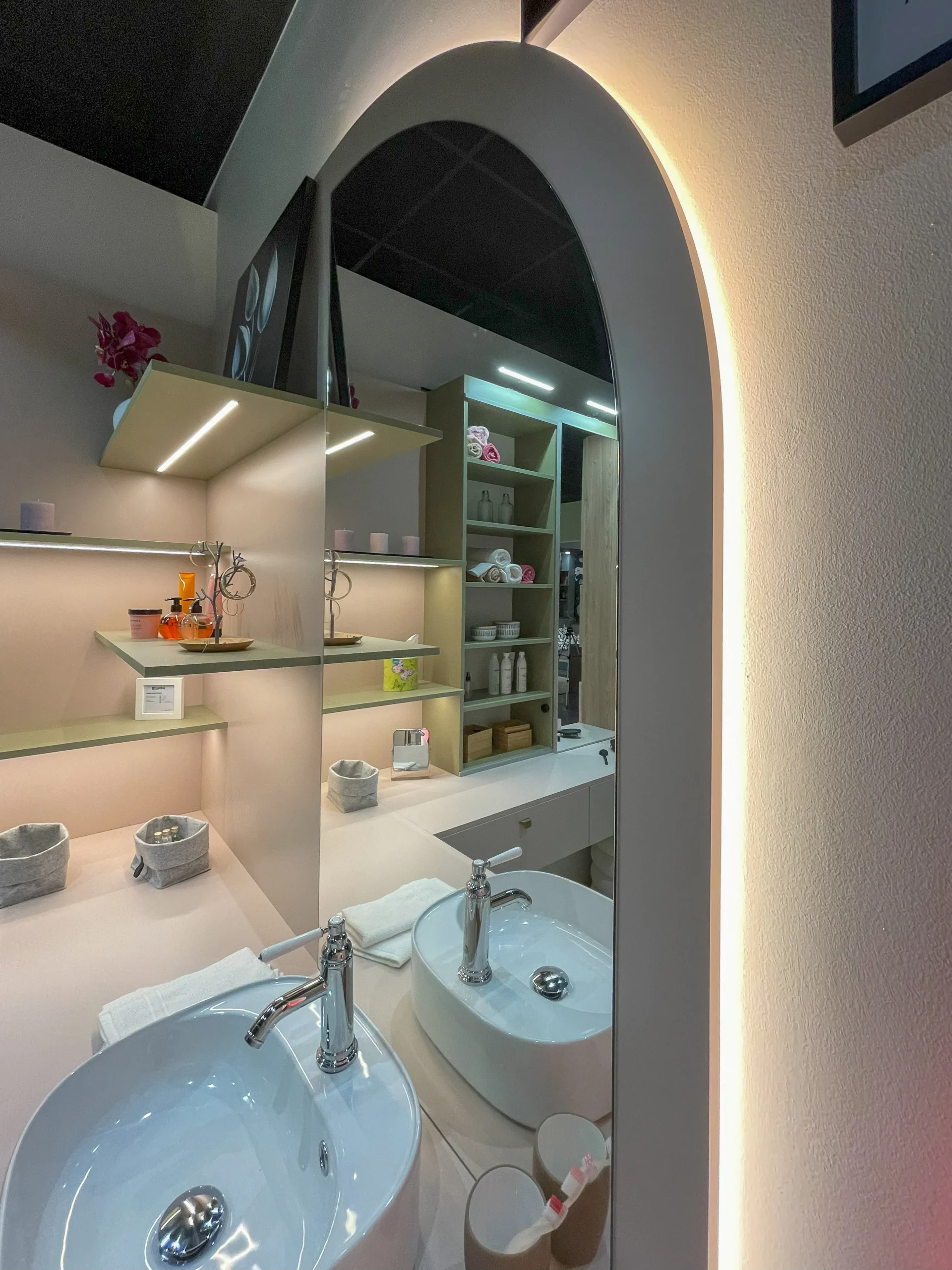 Miroir arrondi rétroéclairé avec vasque posée, étagères murales et rangements de salle de bain sur-mesure.