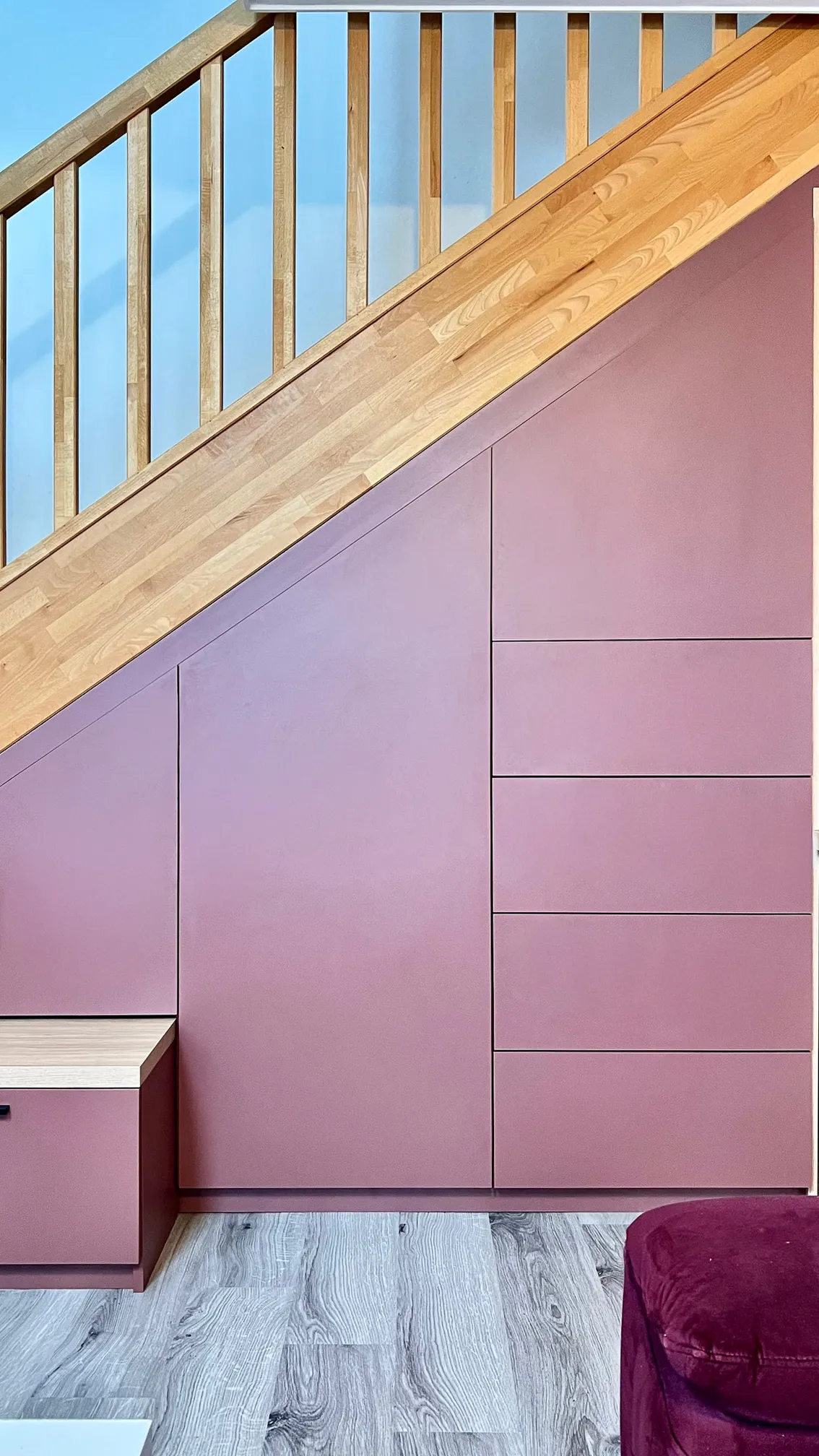 Placard sous escalier sur-mesure avec façades rose poudré, tiroirs intégrés et lignes adaptées à la pente.