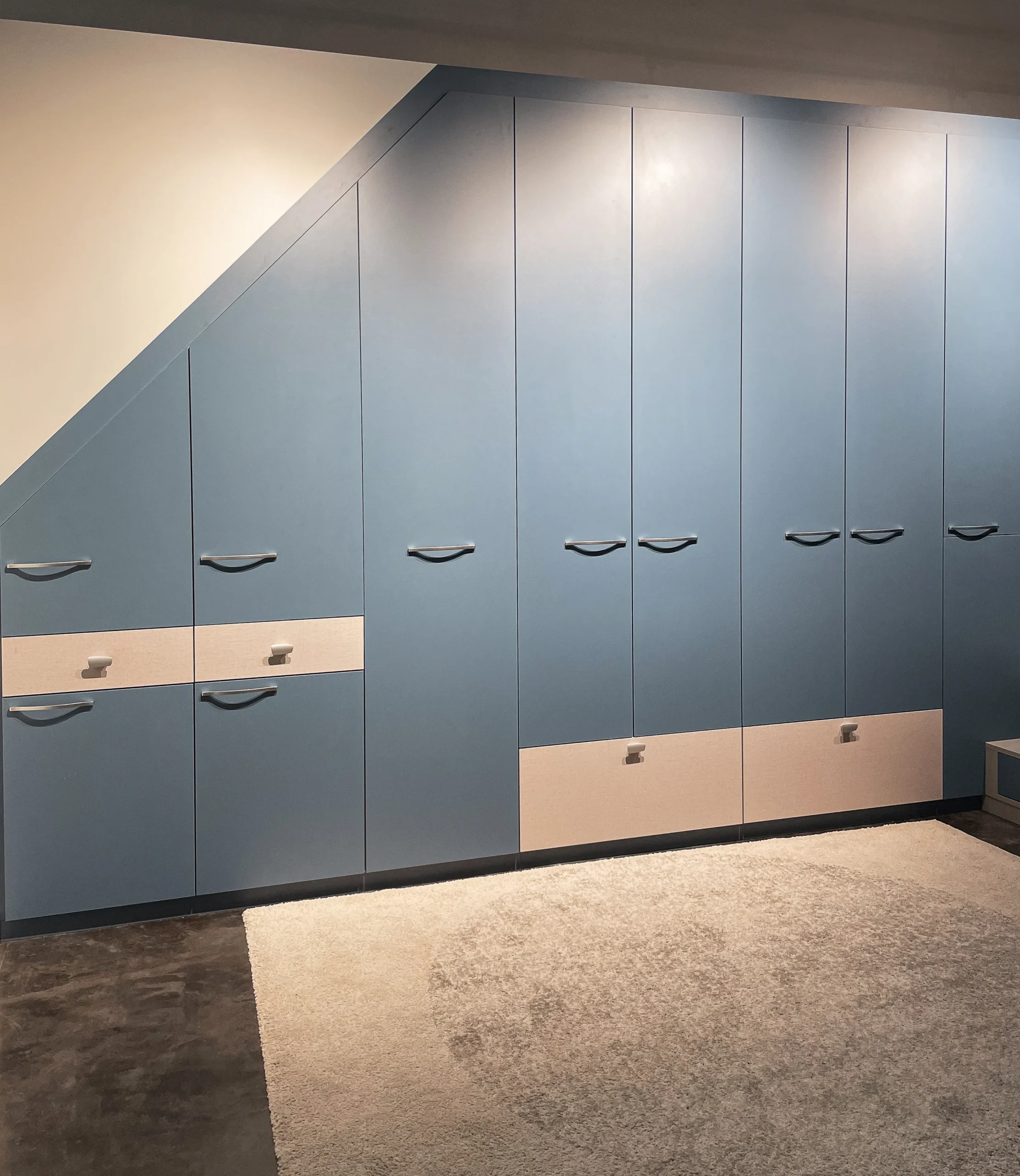 Grand placard sous-pente bleu avec portes battantes, tiroirs bas et finitions claires pour optimiser une chambre enfant.