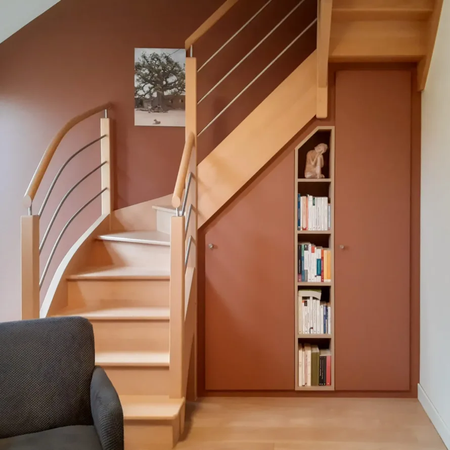 Aménagement sous escalier avec rangements fermés, bibliothèque intégrée et finition terracotta dans un intérieur chaleureux.