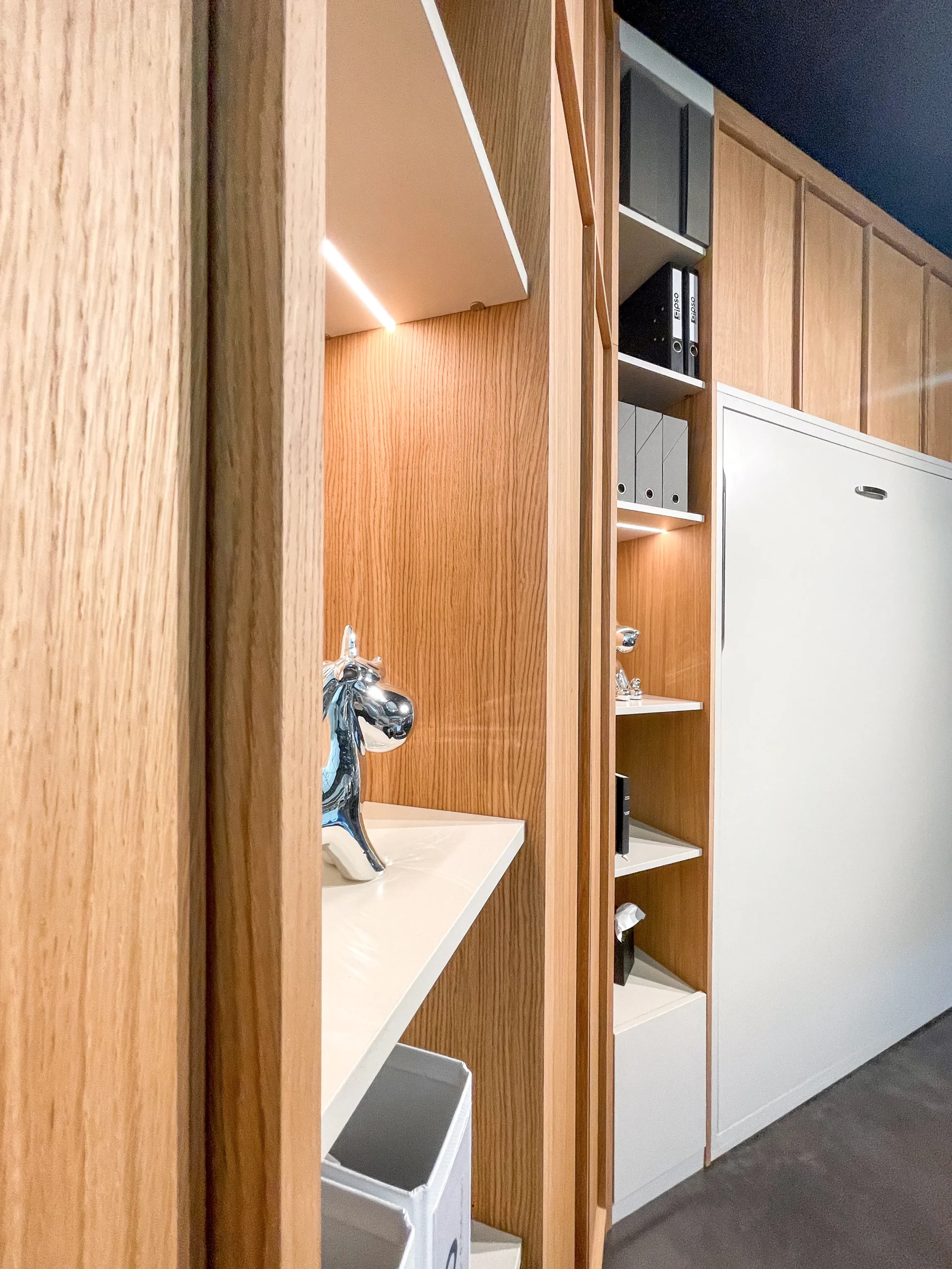 Détail de niches ouvertes éclairées, intégrées à un meuble mural en bois clair autour d’un lit escamotable.