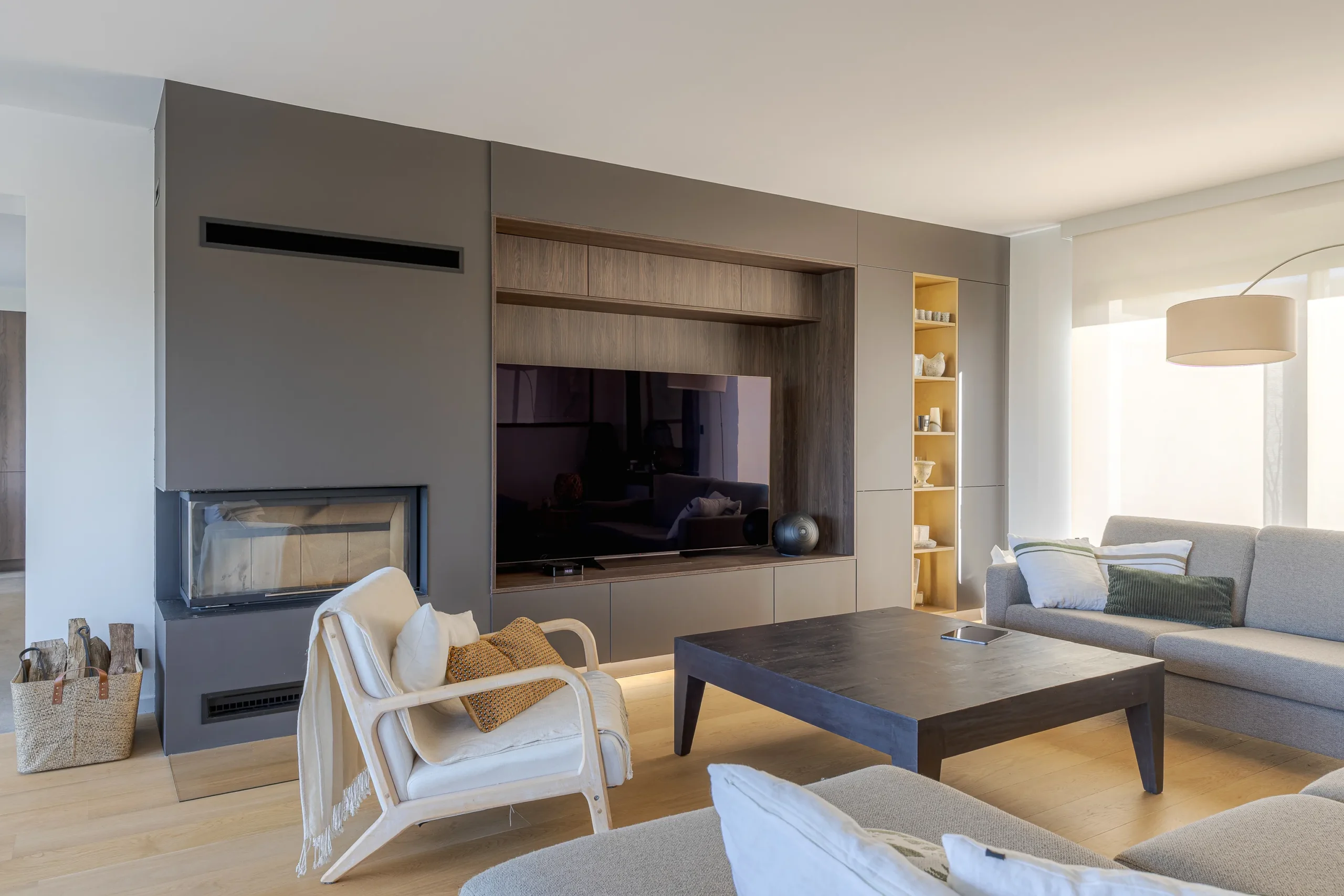 Vue d’ensemble d’un salon lumineux avec meuble TV sur mesure, cheminée contemporaine et rangements intégrés toute hauteur.