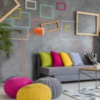 Salon contemporain avec canapé gris, coussins colorés, mur décoratif graphique et lampadaire orange.