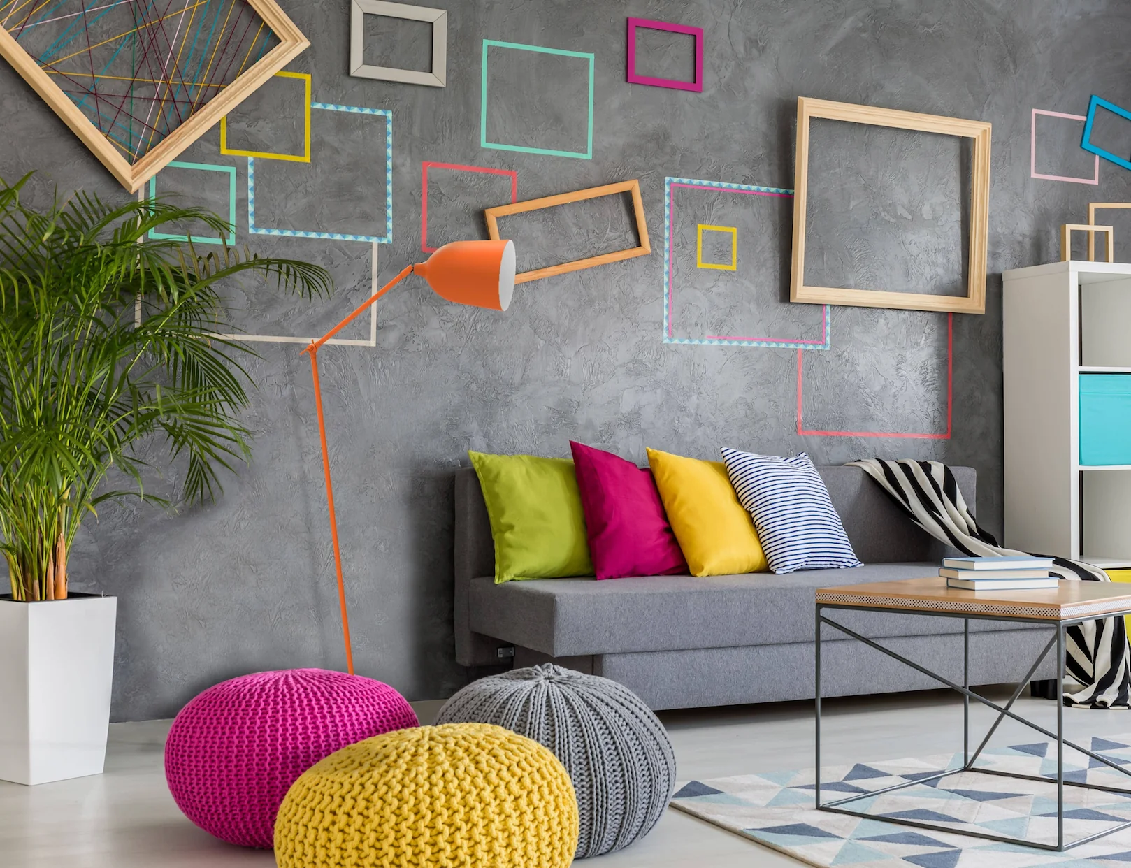 Salon contemporain avec canapé gris, coussins colorés, mur décoratif graphique et lampadaire orange.