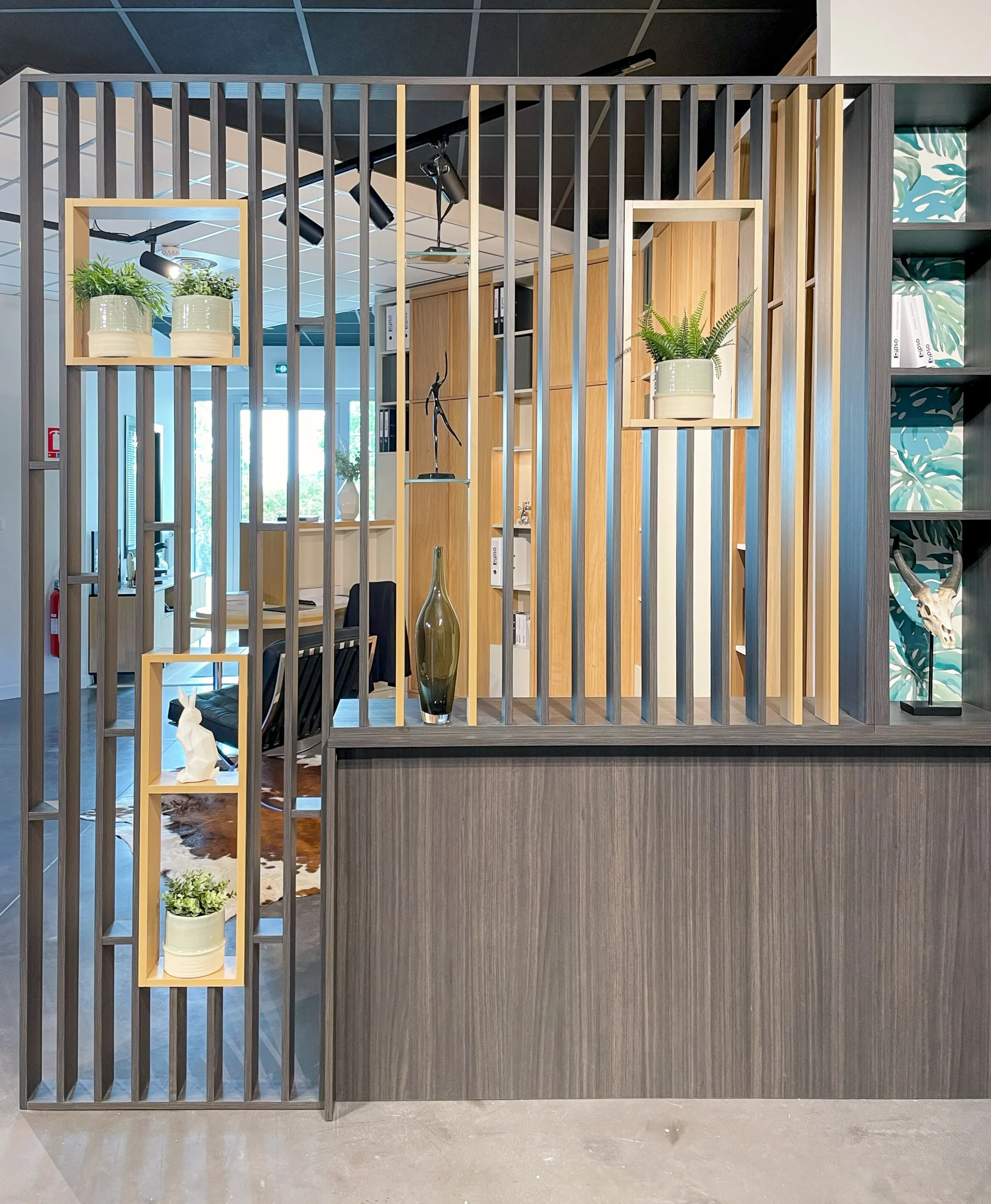 Séparation intérieure ajourée avec tasseaux verticaux, niches intégrées, plantes en pot, vase décoratif et bibliothèque latérale.