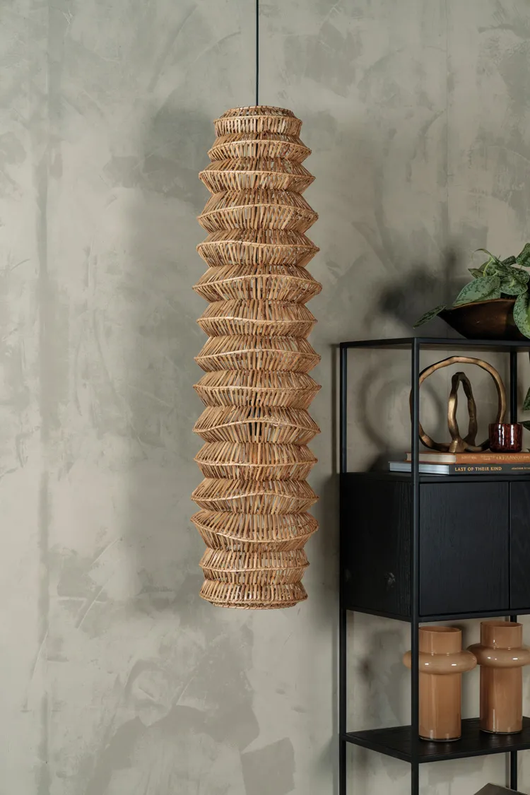 Suspension en fibres naturelles tressées devant un mur texturé, avec mobilier noir et objets décoratifs.