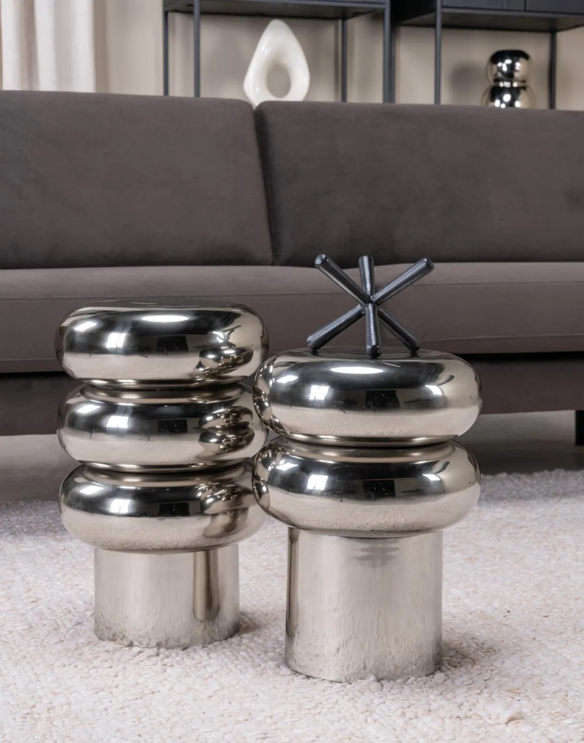 Tables d’appoint chromées aux formes arrondies devant un canapé gris, pour une décoration intérieure moderne et raffinée.