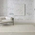 Tapis blanc texturé avec canapé clair et mur en briques blanches, dans un salon minimaliste à l’esprit contemporain.