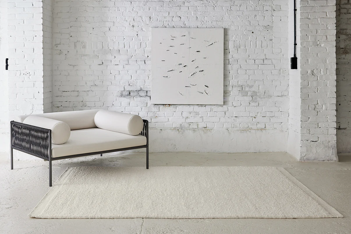 Tapis blanc texturé avec canapé clair et mur en briques blanches, dans un salon minimaliste à l’esprit contemporain.