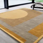 Tapis graphique aux tons beige, gris et jaune dans un salon lumineux avec grandes baies vitrées.