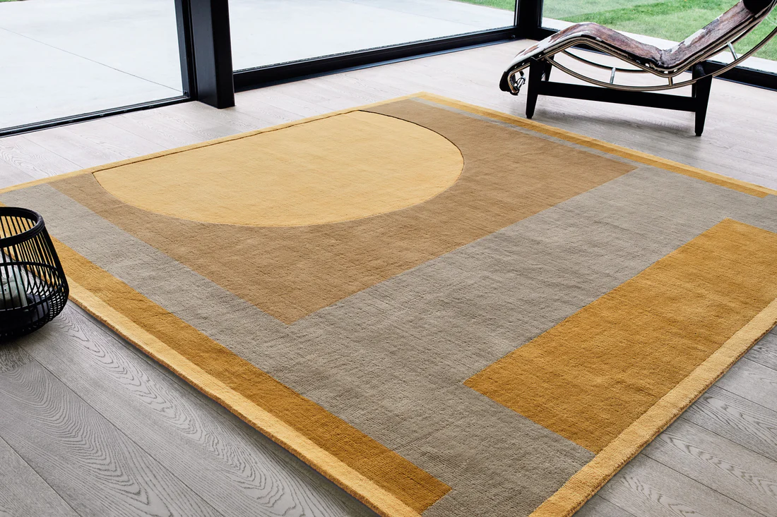 Tapis graphique aux tons beige, gris et jaune dans un salon lumineux avec grandes baies vitrées.